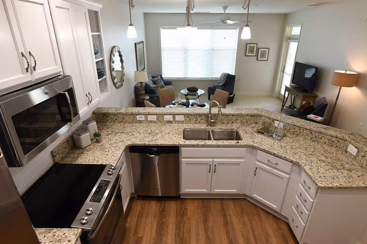 Open modern kitchen with granite countertops, stainless steel appliances and a view into a furnished living room.