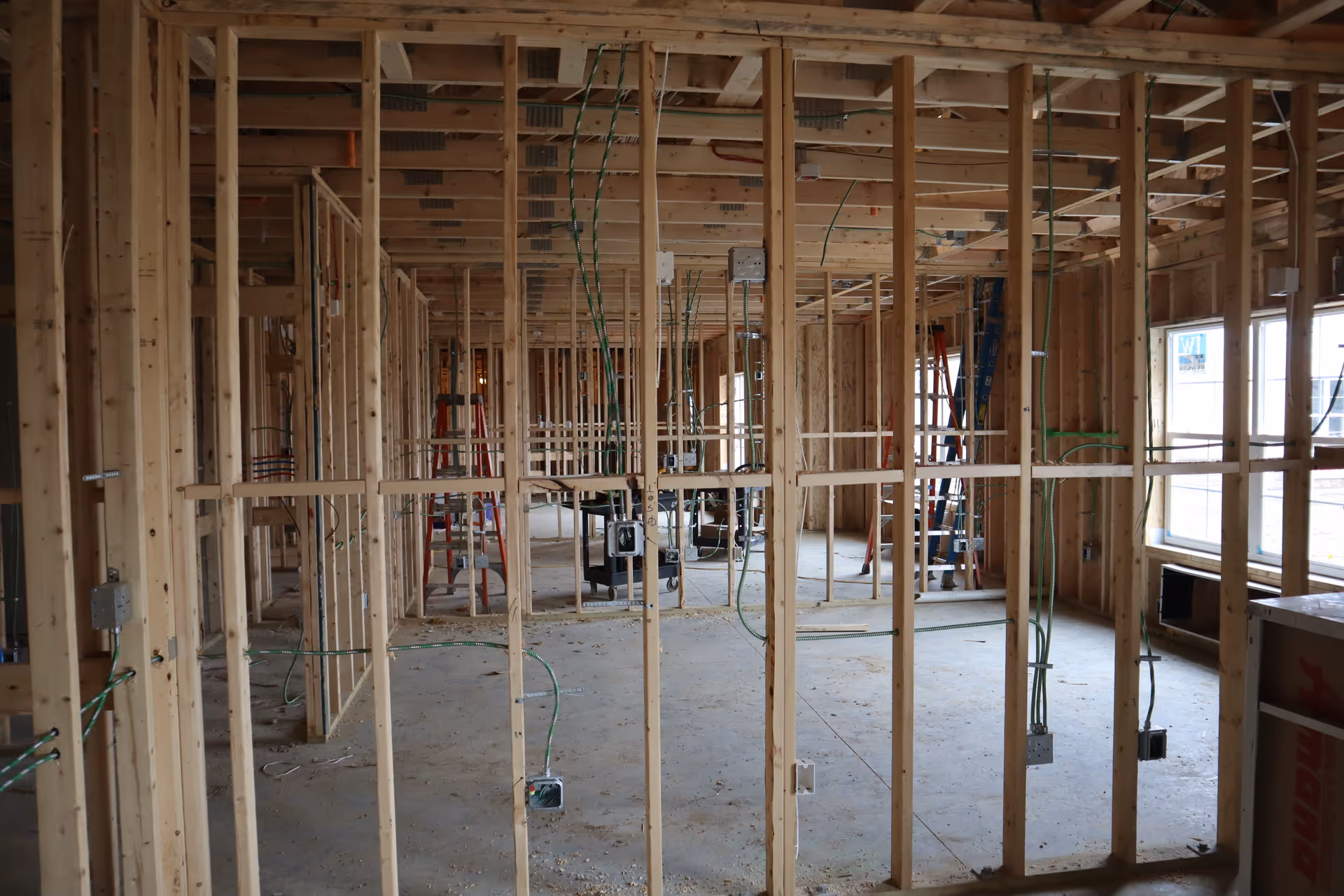 Interior view of a building under construction showing wooden framing, electrical wiring, and ladders.
