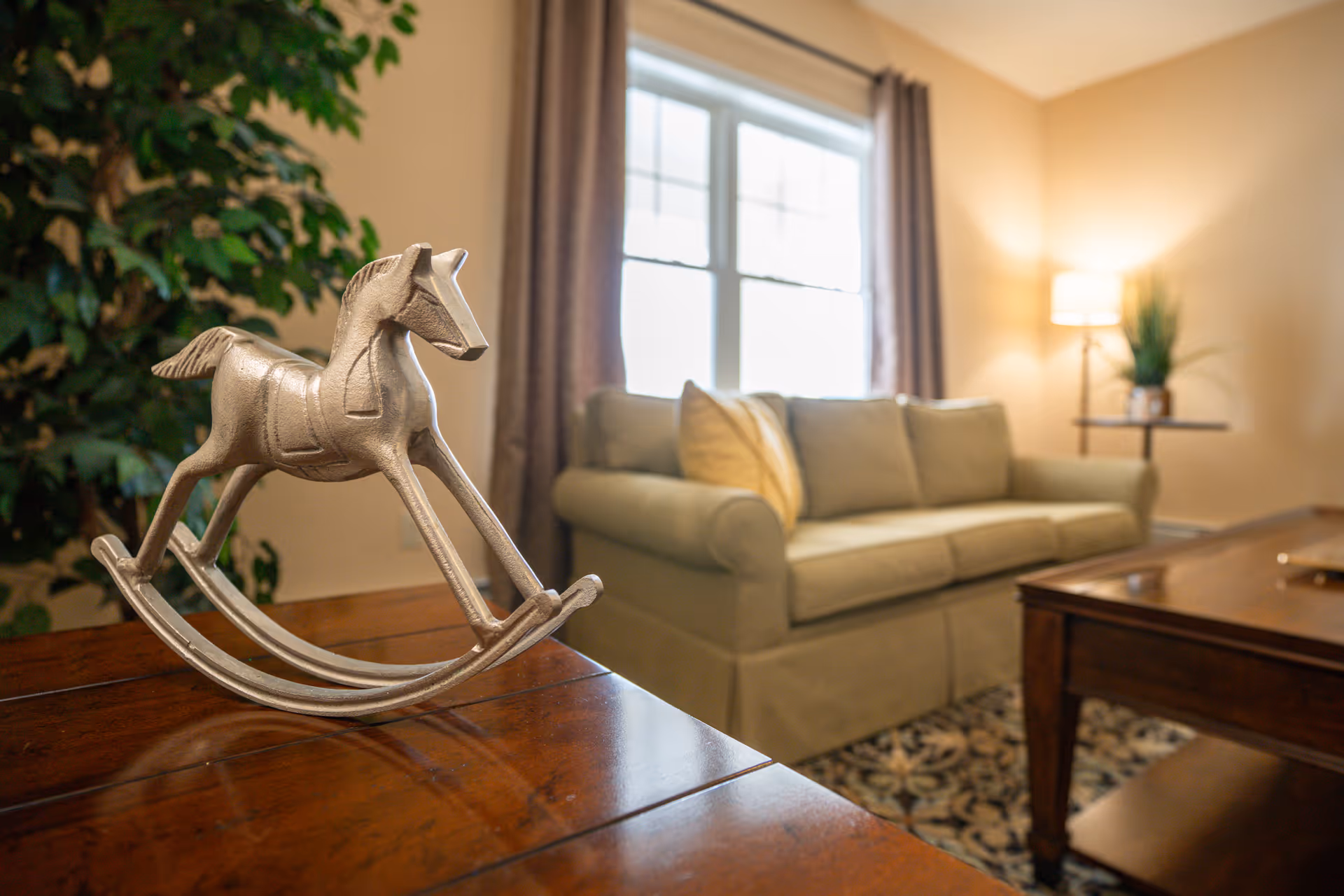 Decorative metal rocking-horse figurine on a wooden table with a sofa and lamp in a well-lit living room.