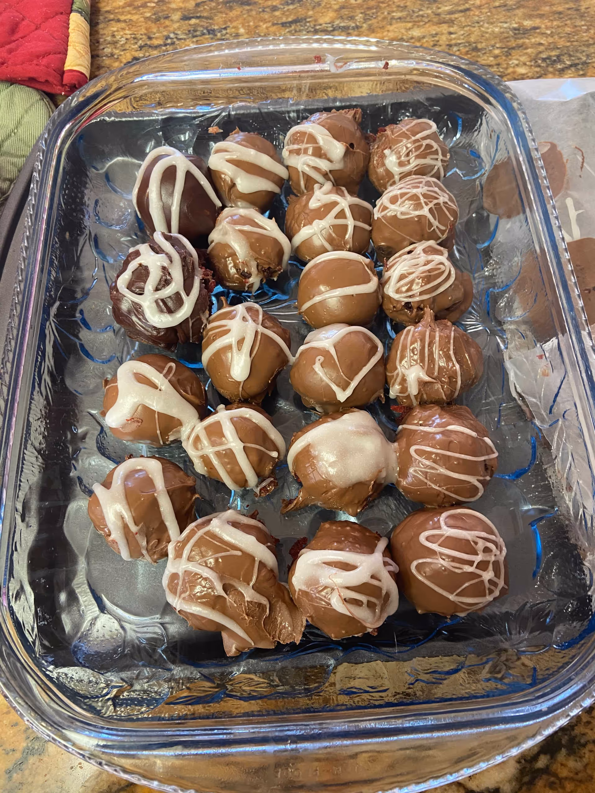 A glass baking dish on a countertop holding chocolate-coated truffle balls drizzled with white icing.