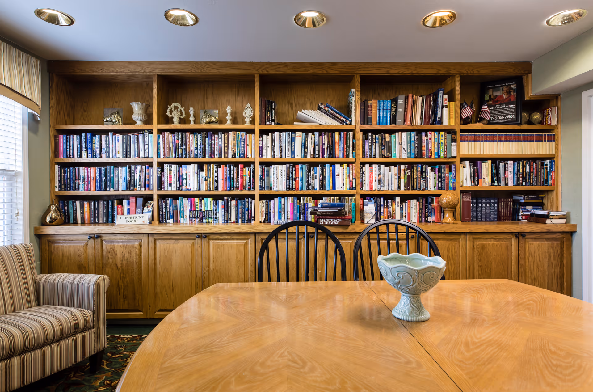 Communal reading room with built-in wooden bookshelves, a large table with chairs and a decorative bowl.