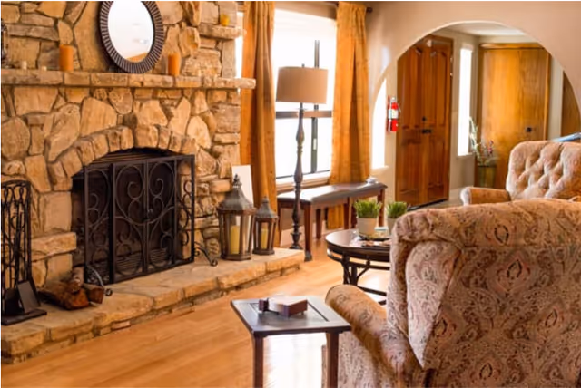 Cozy living room with a stone fireplace, upholstered armchairs, a coffee table, and a wooden entry door.