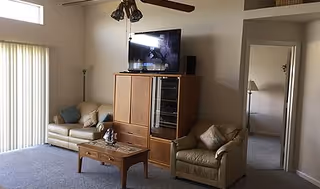 Cozy living room with tan sofas, wooden cabinet, coffee table, TV, and ceiling fan.