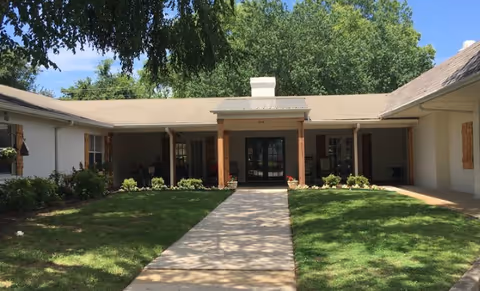 A single-story senior living facility entrance with a covered porch and well-kept lawn.