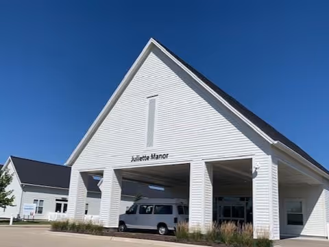 Entrance of a white senior living building labeled "Juliette Manor" with a covered drive-through and a van parked beneath it.