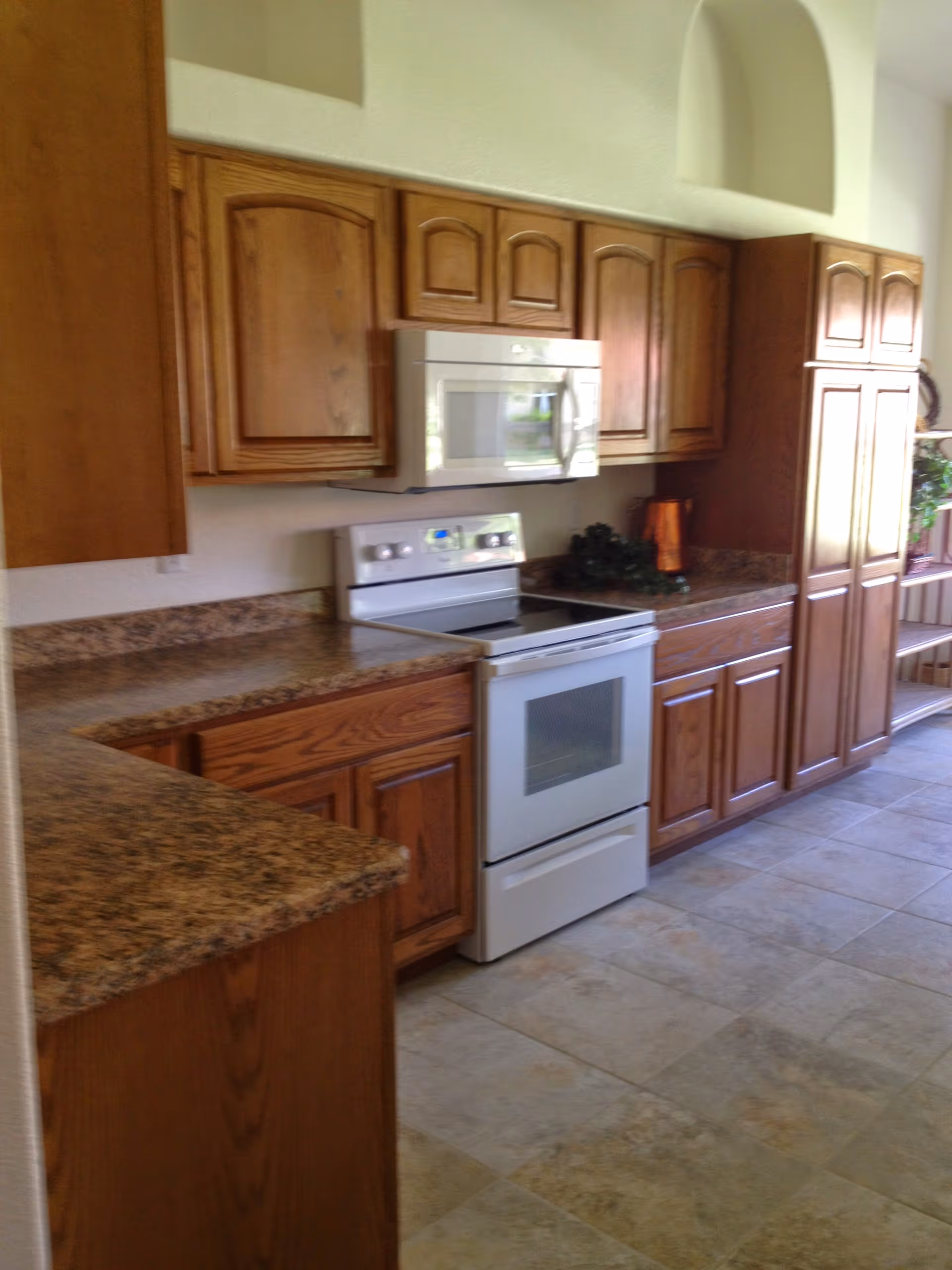 Bright kitchen with wooden cabinets, laminate countertops, a white stove and microwave, and tiled floor.