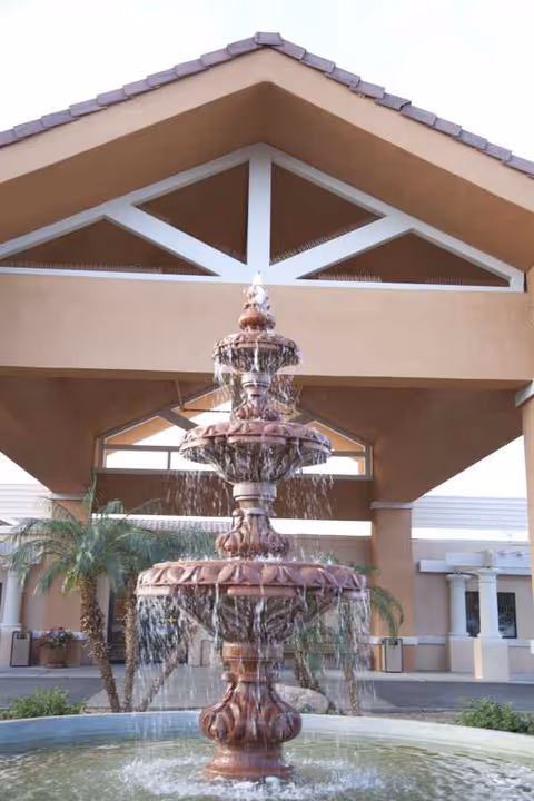 A multi-tier fountain in front of a beige senior living facility entrance.