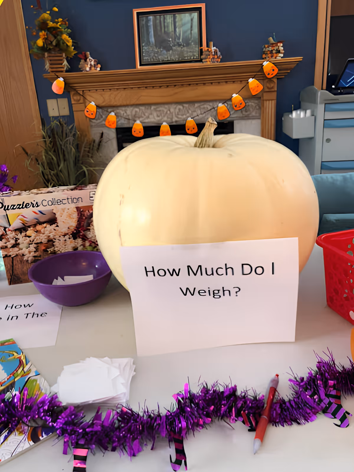 A large pale pumpkin on a table with a sign reading "How Much Do I Weigh?" in a decorated room with a fireplace in the background.
