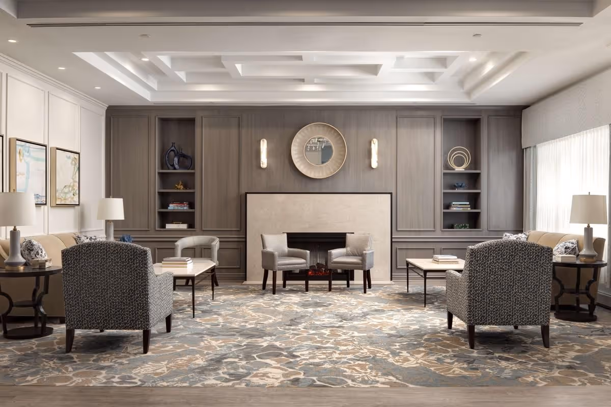 Elegant lounge with armchairs and sofas arranged around a central fireplace, built-in shelving, and soft overhead lighting.