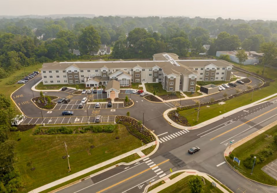 Aerial view of a three-story senior living facility with parking lots, landscaped grounds, and surrounding roads.