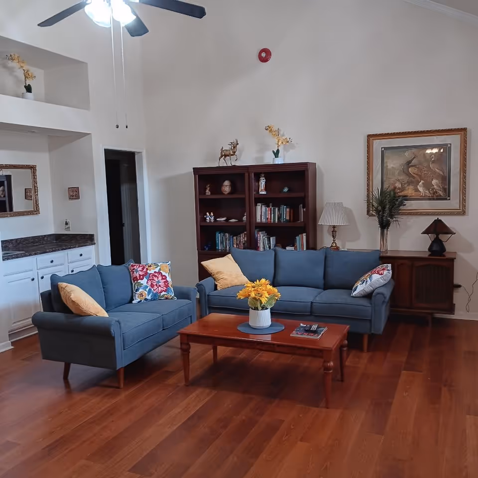 Cozy lounge area with blue couches, a coffee table, bookshelf, and decorative art.