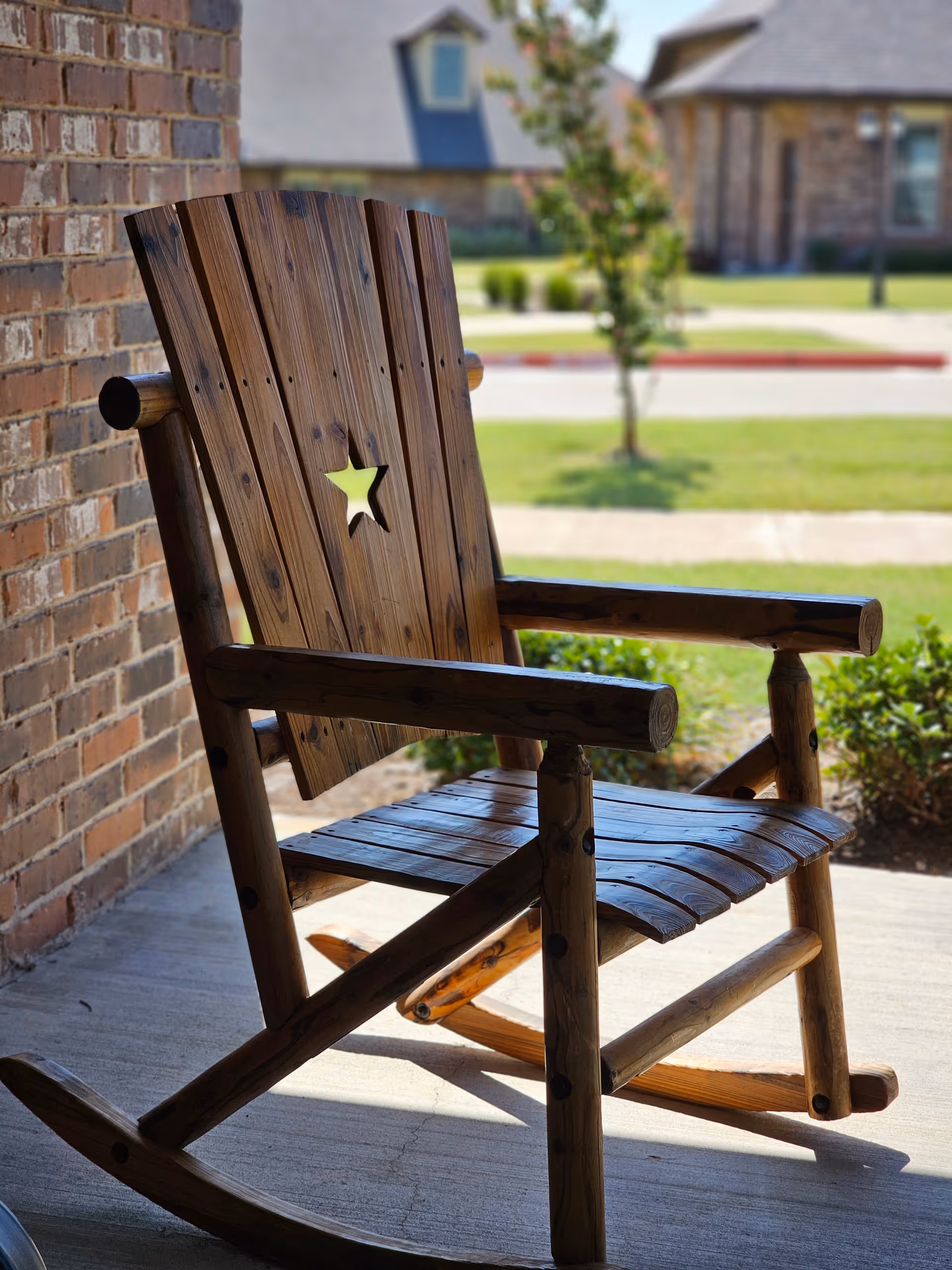 Wooden rocking chair with a star cutout on a porch overlooking a suburban lawn and street.