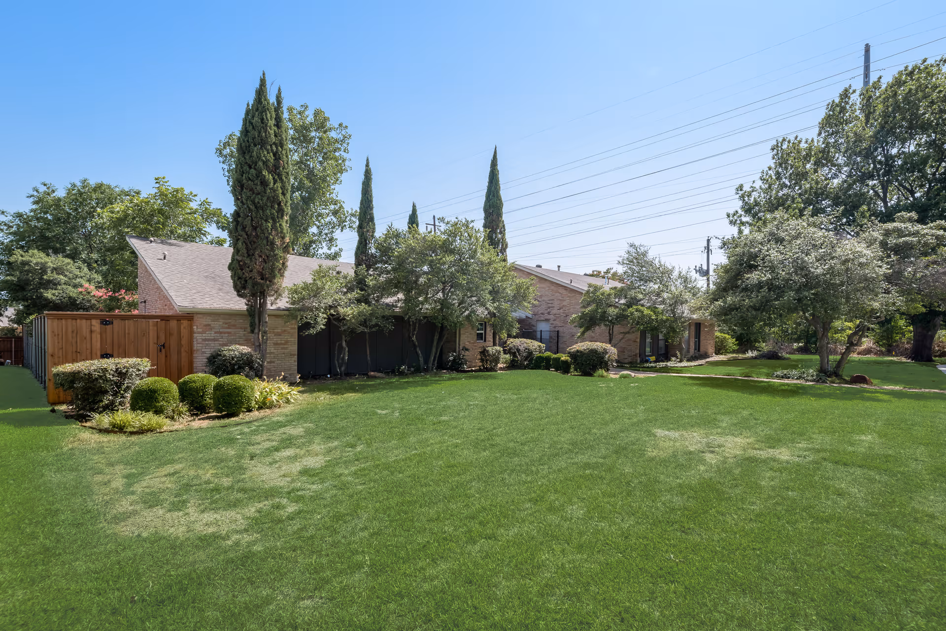 Single-story brick building surrounded by a large green lawn, shrubs and trees under a clear blue sky.
