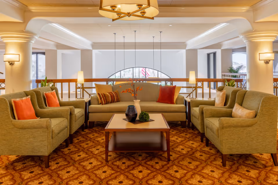 A communal lounge with green sofas and armchairs arranged around a central coffee table under warm lighting.