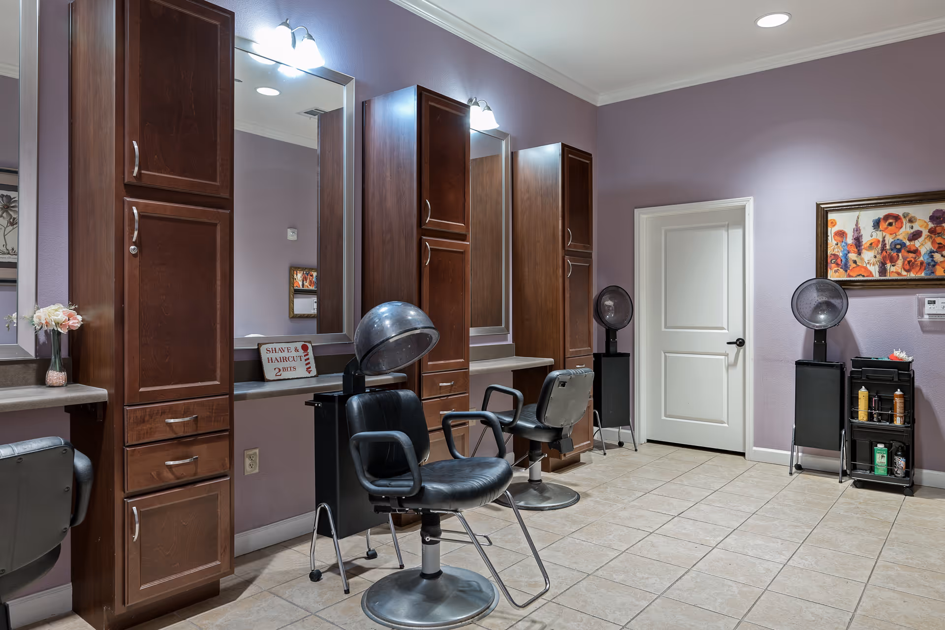 Salon-style room with hair-styling chairs, hooded dryers, mirrors, and tall wooden cabinets against lavender walls.
