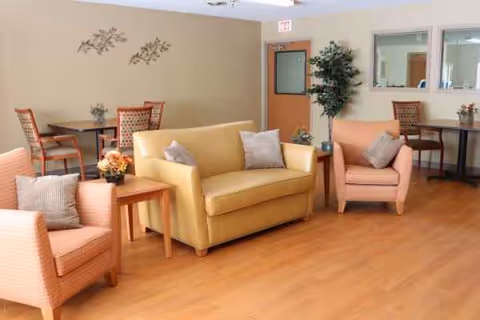 Cozy lounge area in a senior residence with yellow sofa, peach chairs, and wooden tables.