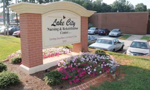 Lake City Nursing & Rehabilitation Center sign with colorful flowers and a parking lot.