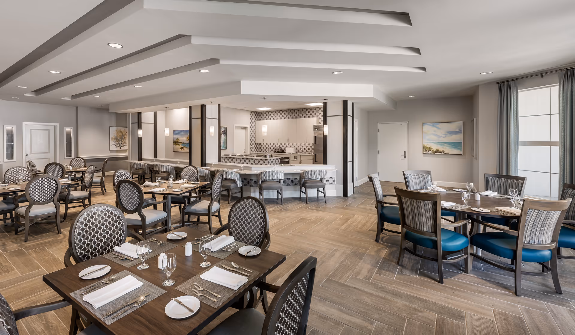 Spacious, well-lit dining room with multiple set tables, upholstered chairs, and a serving counter.