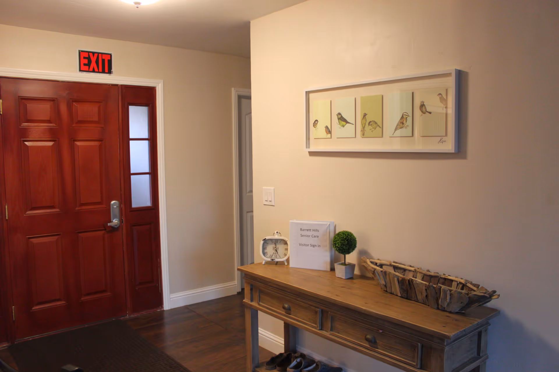 Entryway with a red exit door and a wooden console table holding decorative items and a visitor sign.