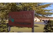 Shenandoah Senior Living Community sign on a lawn with trees and a building in background.