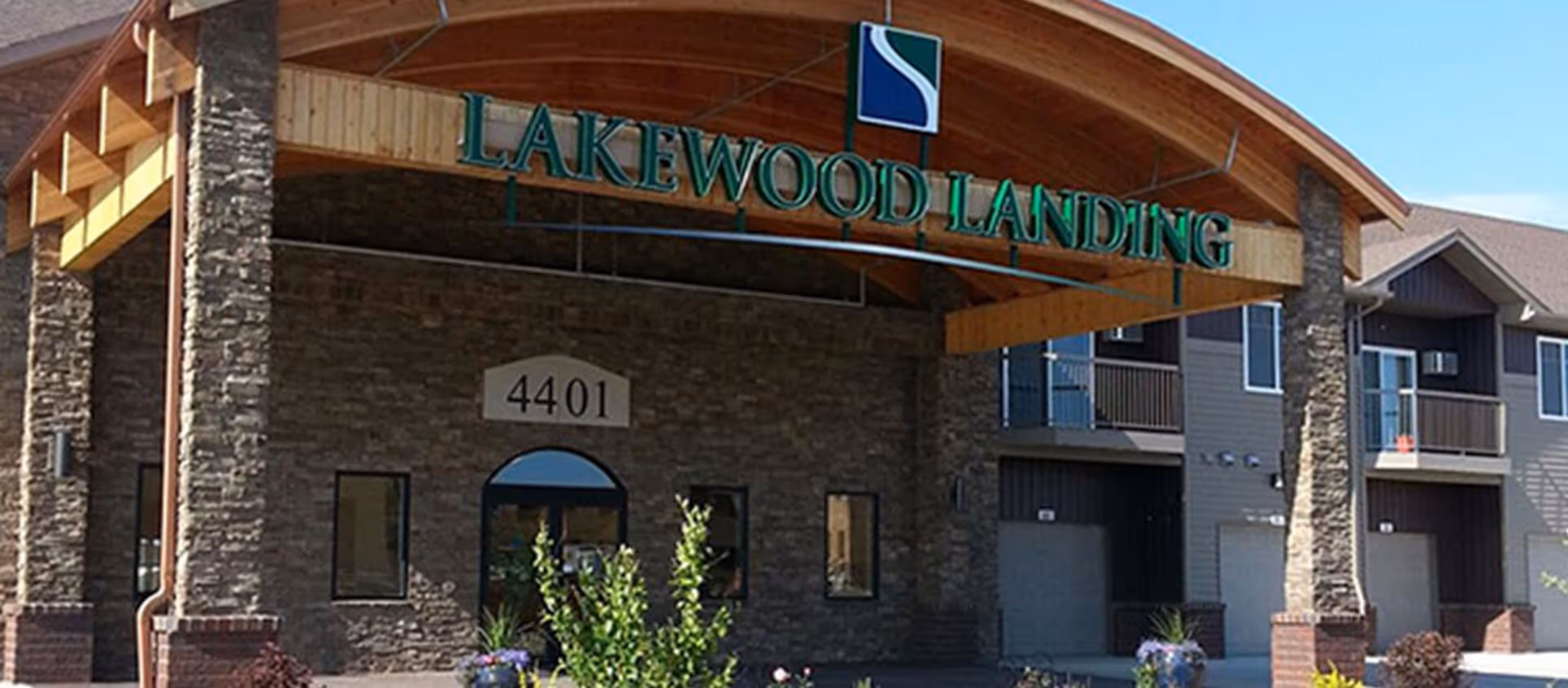 Front exterior view of Lakewood Landing facility with stone pillars, wooden archway, and the address number 4401 displayed above the entrance door.