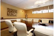 Meeting room with a polished wooden conference table surrounded by white leather chairs and a chandelier-style ceiling light.