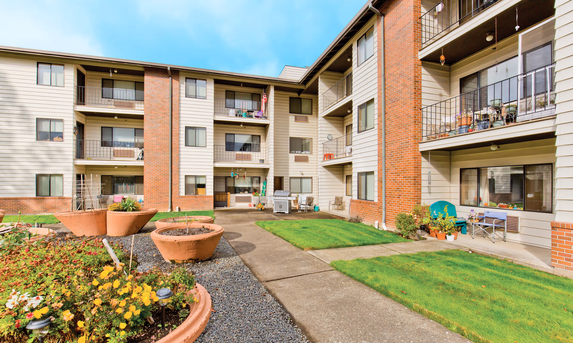 Courtyard and exterior of a three-story senior living apartment building with balconies, planters, and a central walkway.
