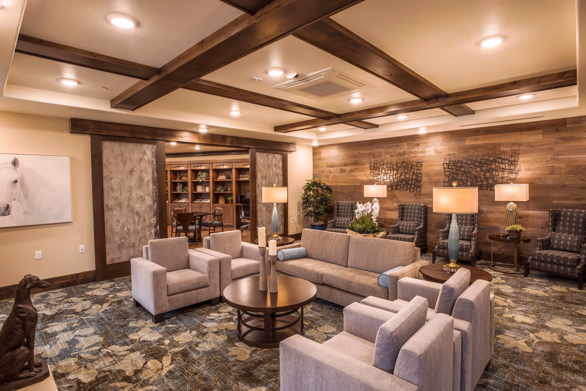 A warm communal lounge with sofas, armchairs, coffee tables and wood-accented walls and ceiling beams.