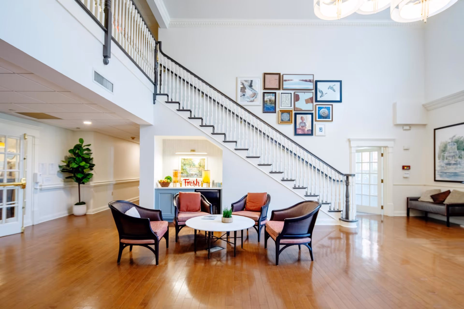 Bright communal lobby with a central seating area, staircase, and framed artwork on the wall.