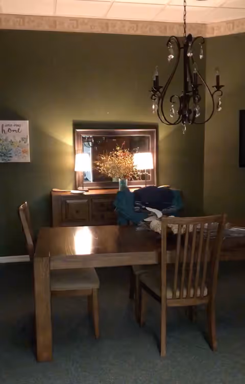 A dining room with a wooden table and chairs, a sideboard with a mirror and lamps, and a hanging chandelier.