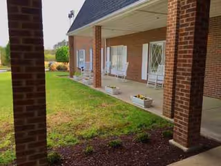 Brick front porch with rocking chairs and white doors overlooking a grassy lawn.