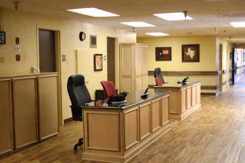 Reception desk area inside a senior living facility with chairs, wooden cabinets, and a hallway.