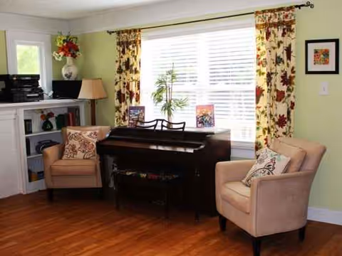 A cozy living room in a residential care home featuring a piano and two beige chairs.