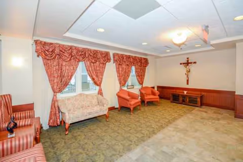 A spacious lounge area with red chairs, drapes, and a crucifix on the wall.