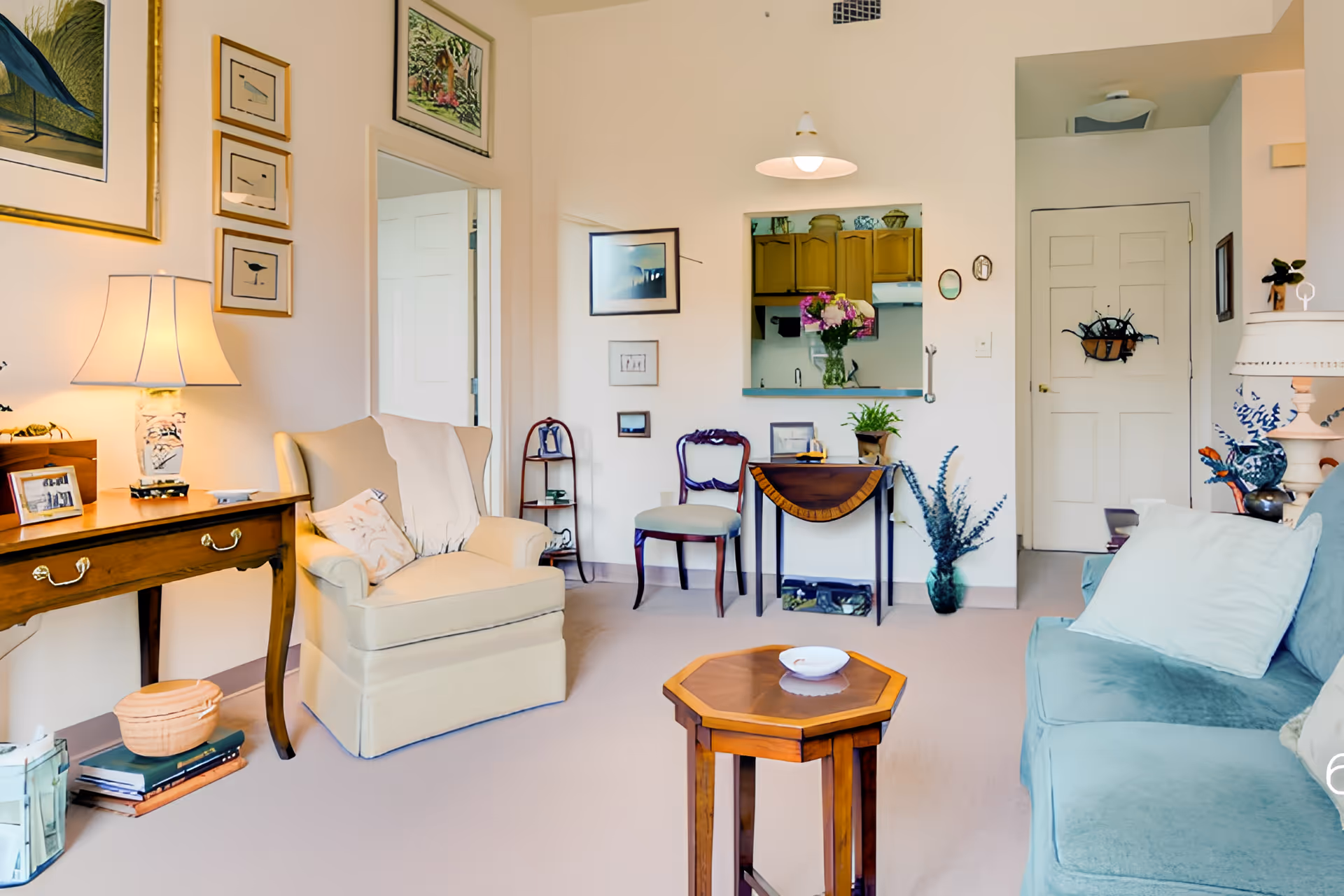 A bright furnished living room with armchairs, a sofa, side tables, lamps, and wall art.