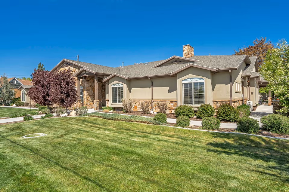 Single-story senior living home with stone accents, manicured lawn, and paved walkways.