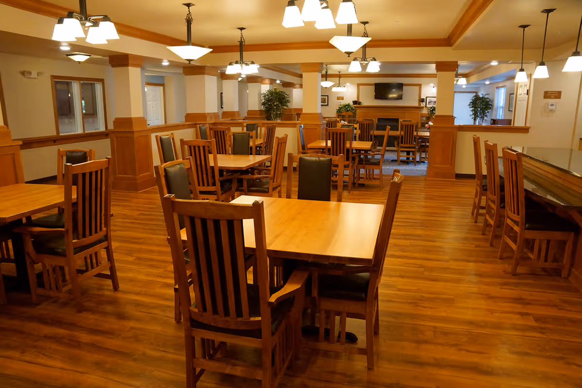 Spacious communal dining room with wooden tables and chairs, pendant lights, and a TV above a fireplace.