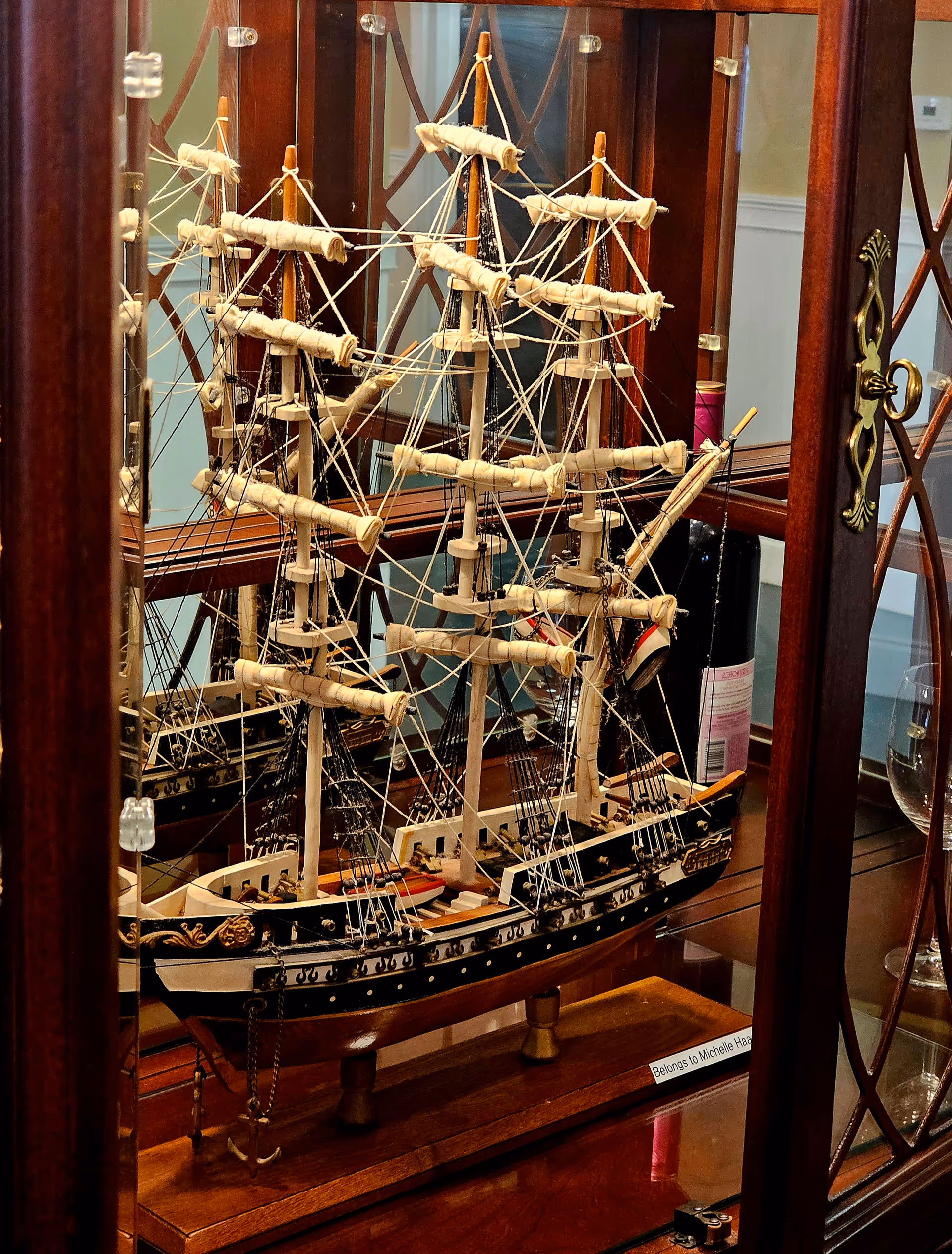 A detailed model sailing ship displayed inside a glass-front wooden cabinet.