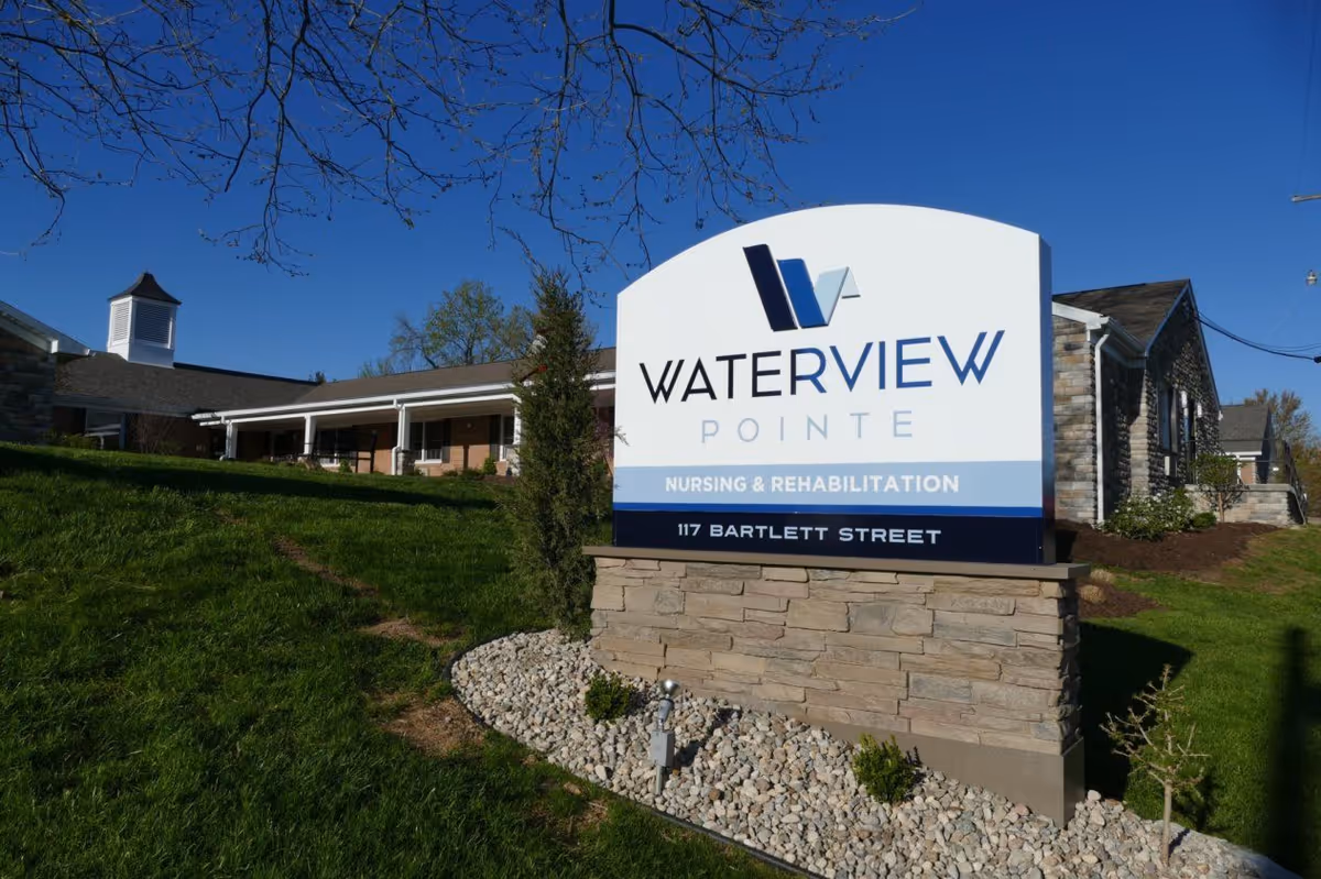 Outdoor view of Waterview Pointe nursing and rehabilitation facility sign with the building and green lawn in the background under a clear blue sky.