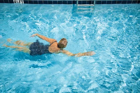 A person swimming face down in a bright blue pool near a metal ladder and a 4½ ft depth marker.