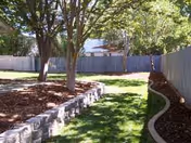 Well kept grassy outdoor area with trees, curved stone edge, and a wooden fence.