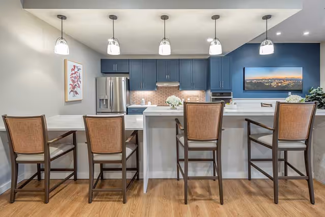 Modern open kitchen with a white island and four bar chairs facing blue cabinets and pendant lights.