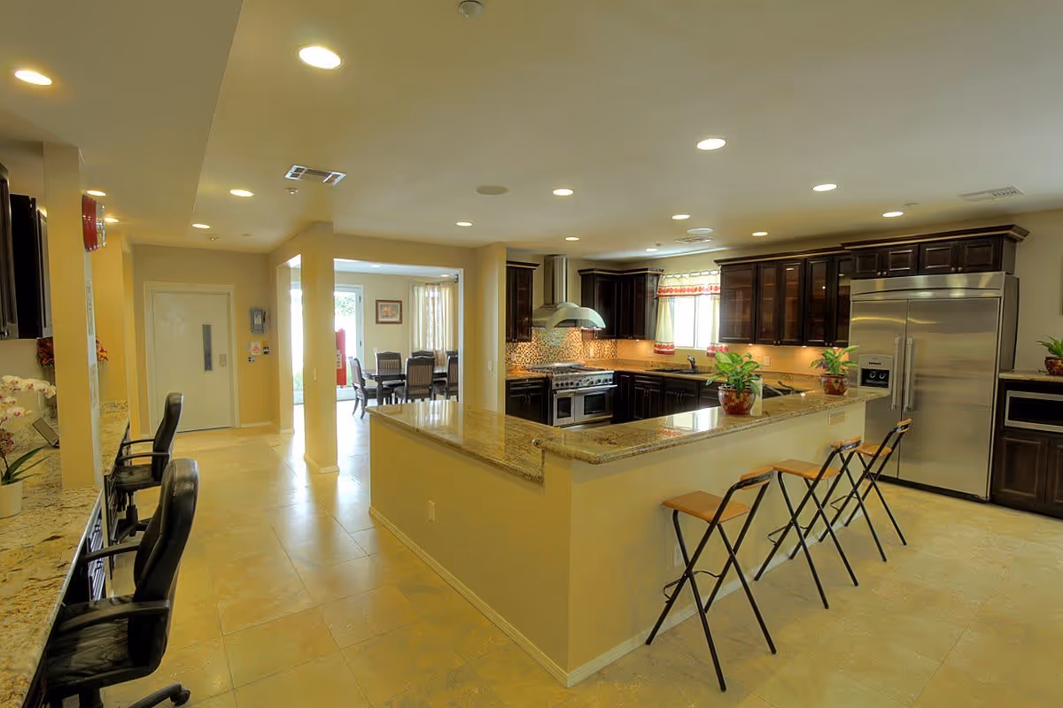 Spacious kitchen with a large island, granite countertops, bar stools, stainless steel appliances, and dark wood cabinets.