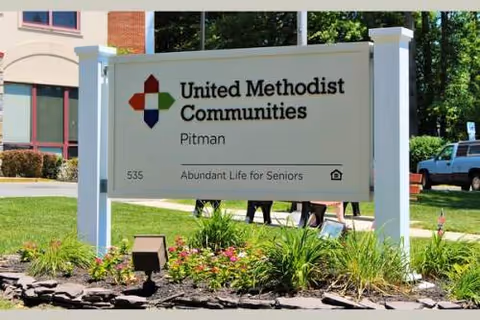 Exterior sign for United Methodist Communities at Pitman with landscaping and a building in background.