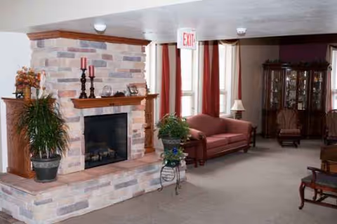 Cozy senior living room with a stone fireplace, red couch, and plants.