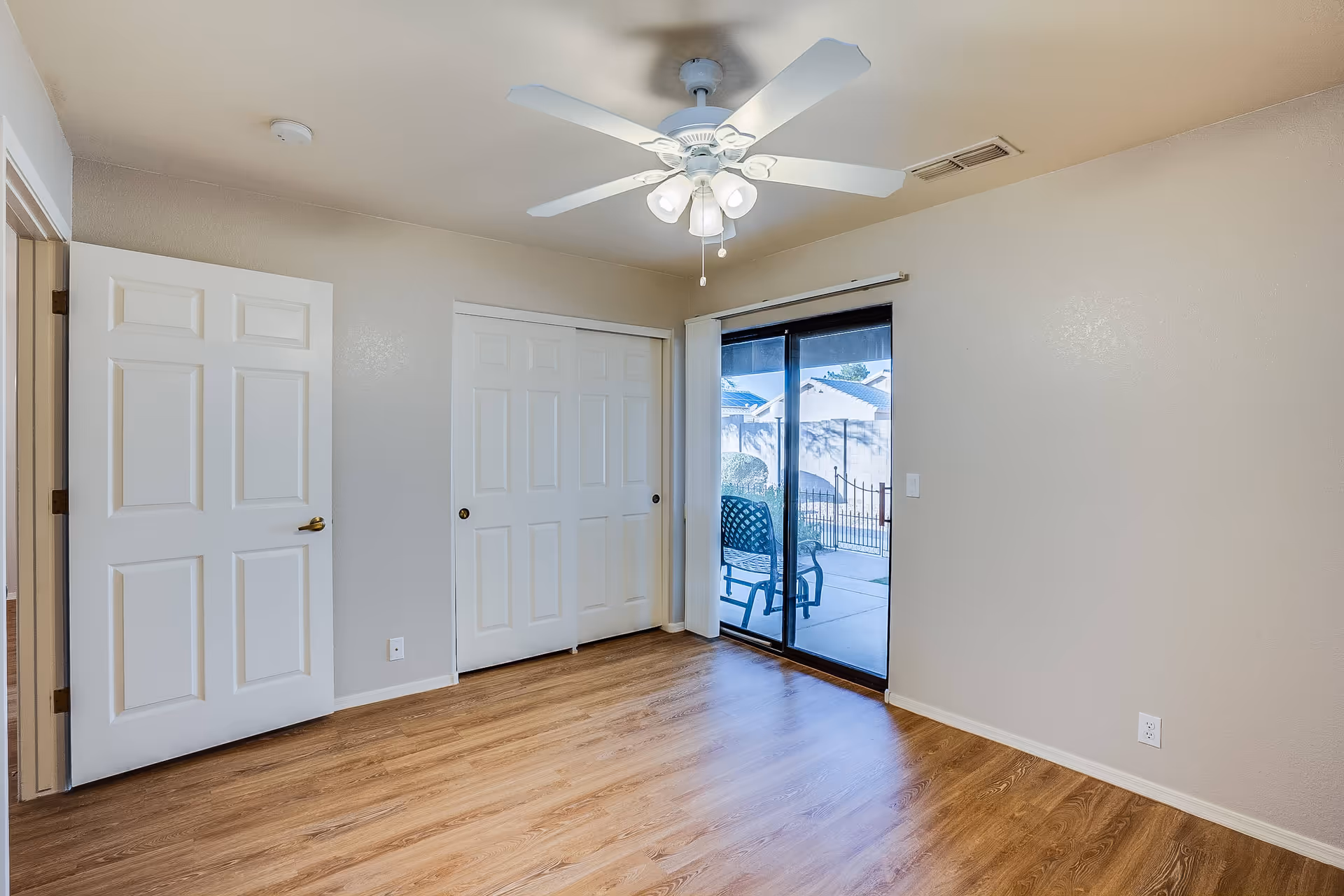 Empty bedroom with wood flooring, a ceiling fan, closet with sliding doors and a glass sliding door opening to a patio.