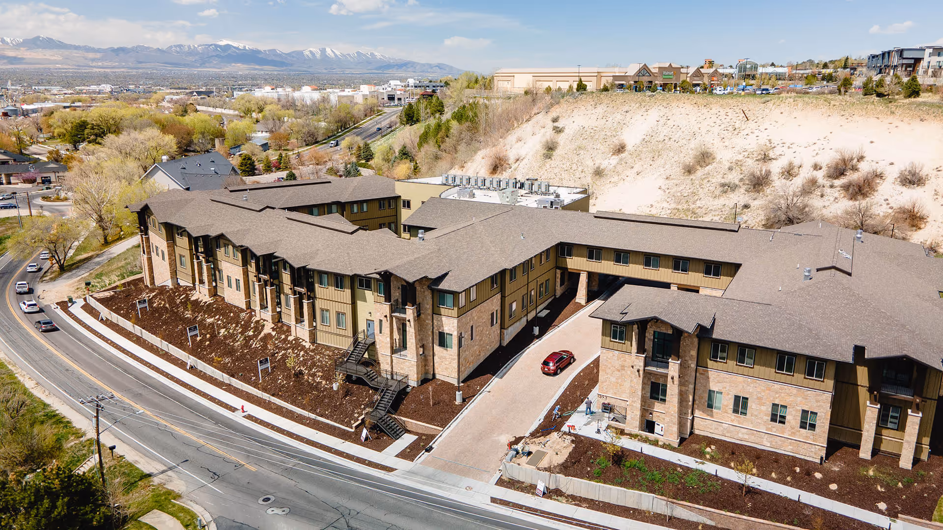 Aerial view of Spring Gardens Senior Living Draper building complex on hillside with mountains.