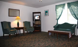 Living room with green seating, coffee table, lamp, TV, and window drapes.