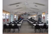 Empty dining hall with long tables, black chairs, and bunting along windows.