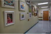 Interior hallway with framed artwork on the left wall, glossy floor, and a door at the corridor end.